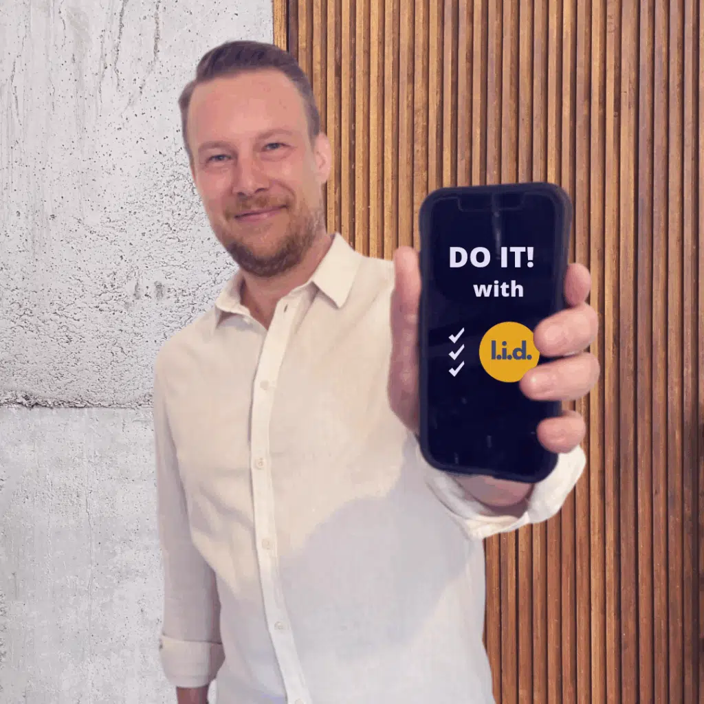 Tobias Hombach hält ein Smartphone mit der Aufschrift „DO IT! with l.i.d.“ und dem l.i.d.-Logo in die Kamera.